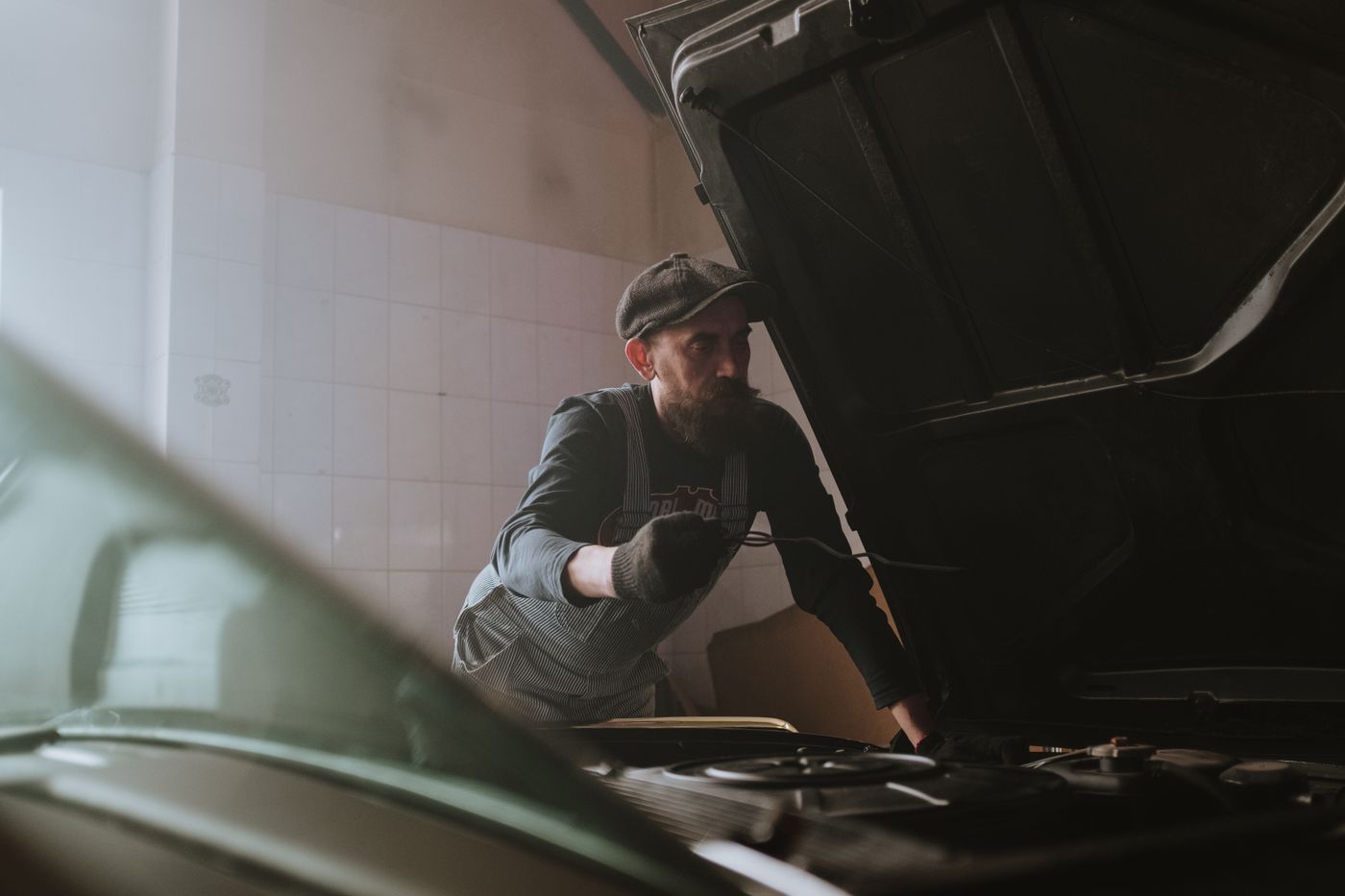 A mechanic leaning under the open bonnet of a car in a workshop.